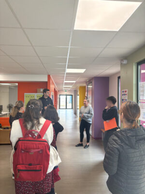 Un groupe d'élèves et enseignants discutent dans un couloir d'école coloré, dos tournés vers la caméra.