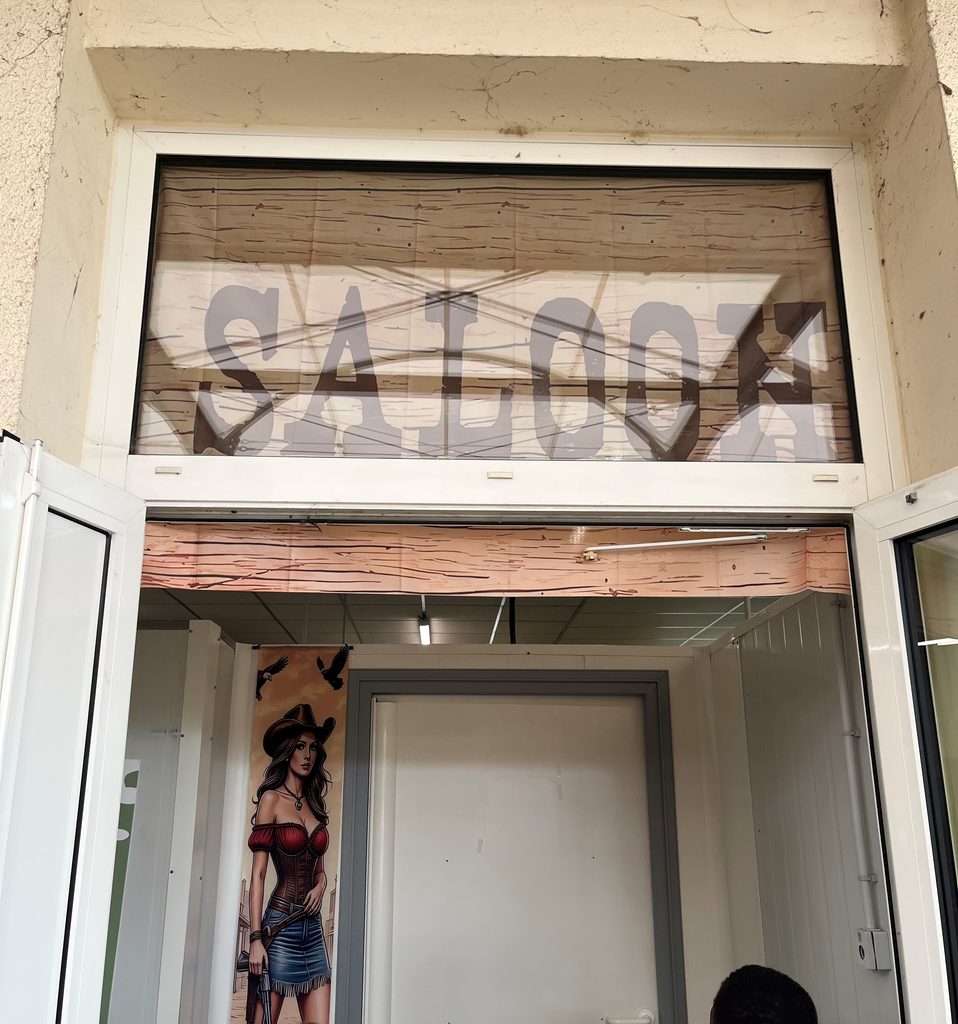 Mural représentant une femme cowgirl devant une enseigne "Saloon" avec décor en bois vieilli.