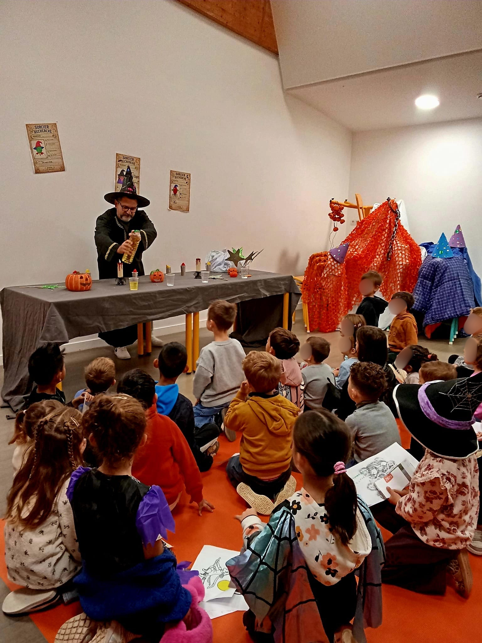 Enfants assis écoutant un sorcier lors d’un atelier Halloween, décorations festives autour.
