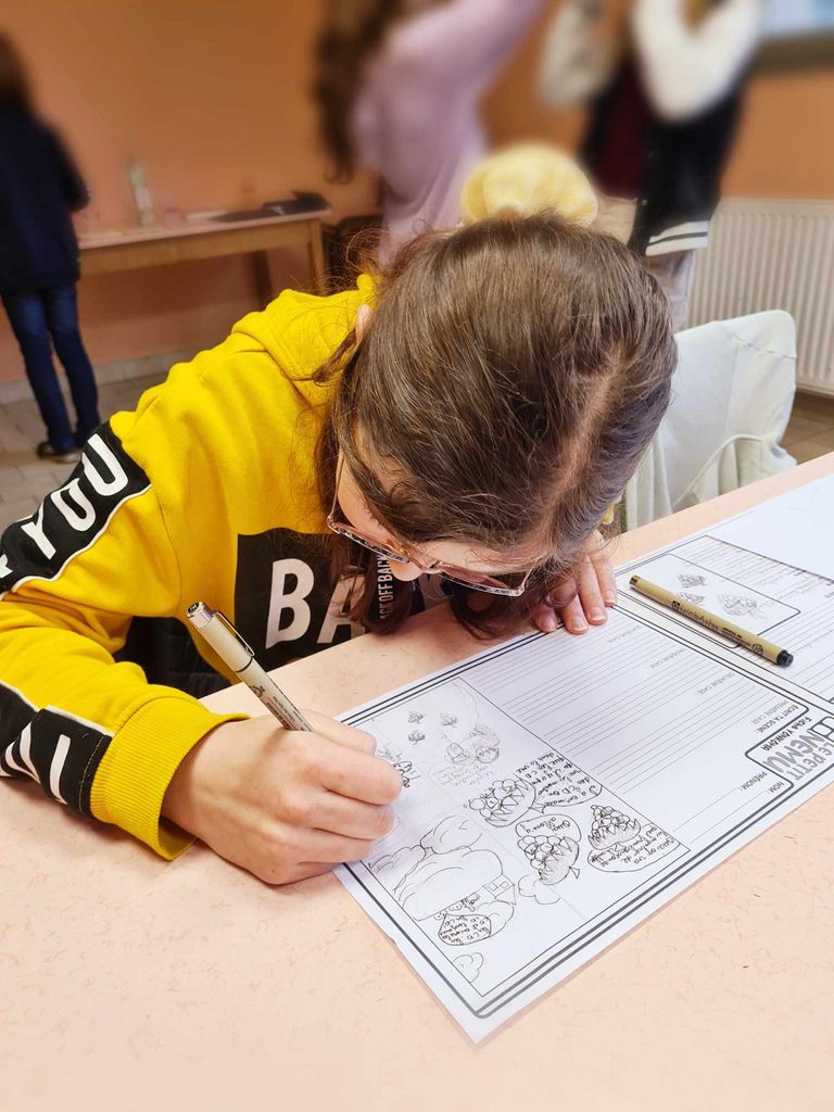 Une enfant en jaune écrit dans un cahier d’activités avec des dessins à compléter, assis à une table.