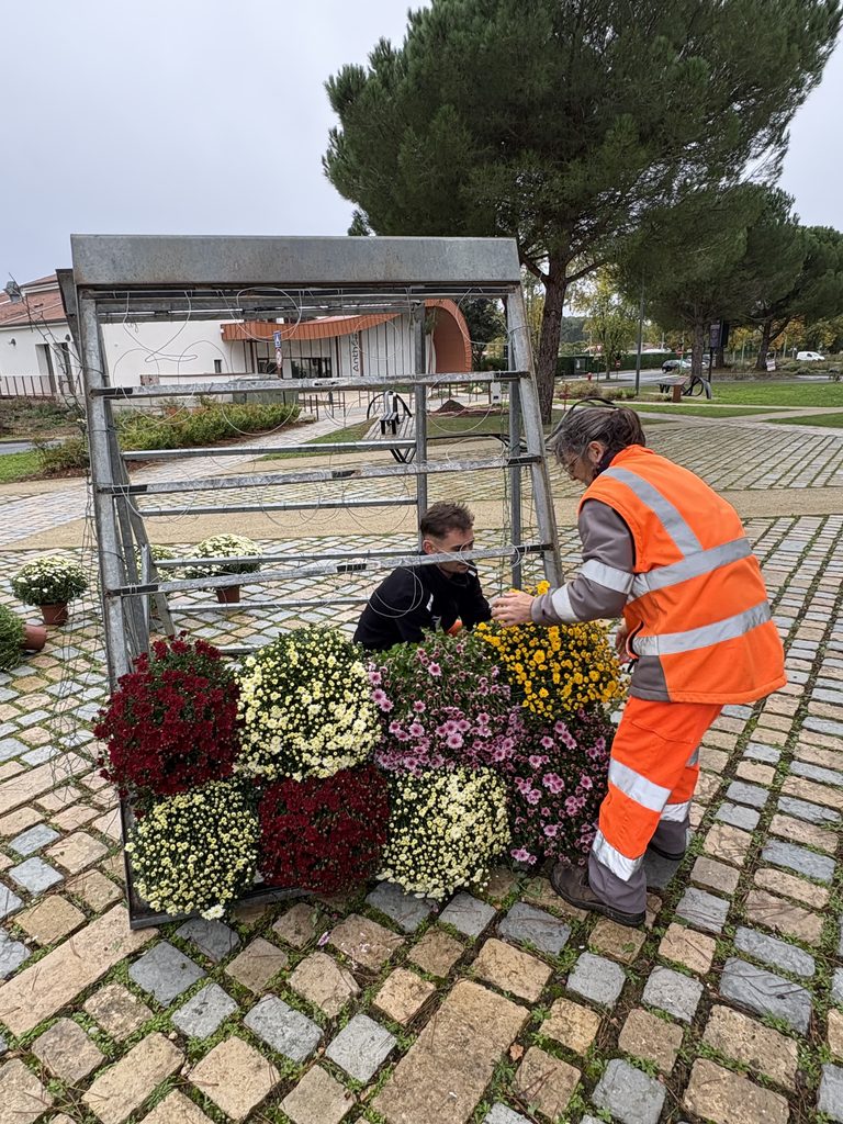 Deux personnes arrangent des fleurs colorées dans un cadre métallique en extérieur, vue de dessus.