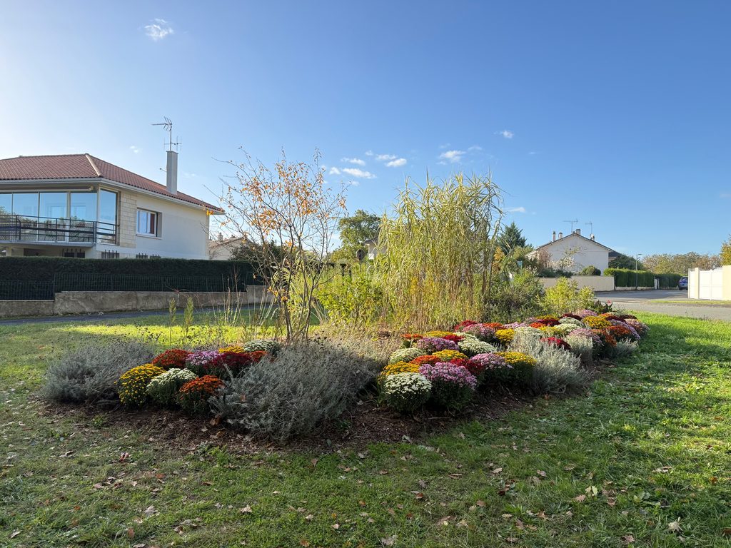 Jardin fleuri avec parterres colorés devant une maison moderne, sous un ciel dégagé.