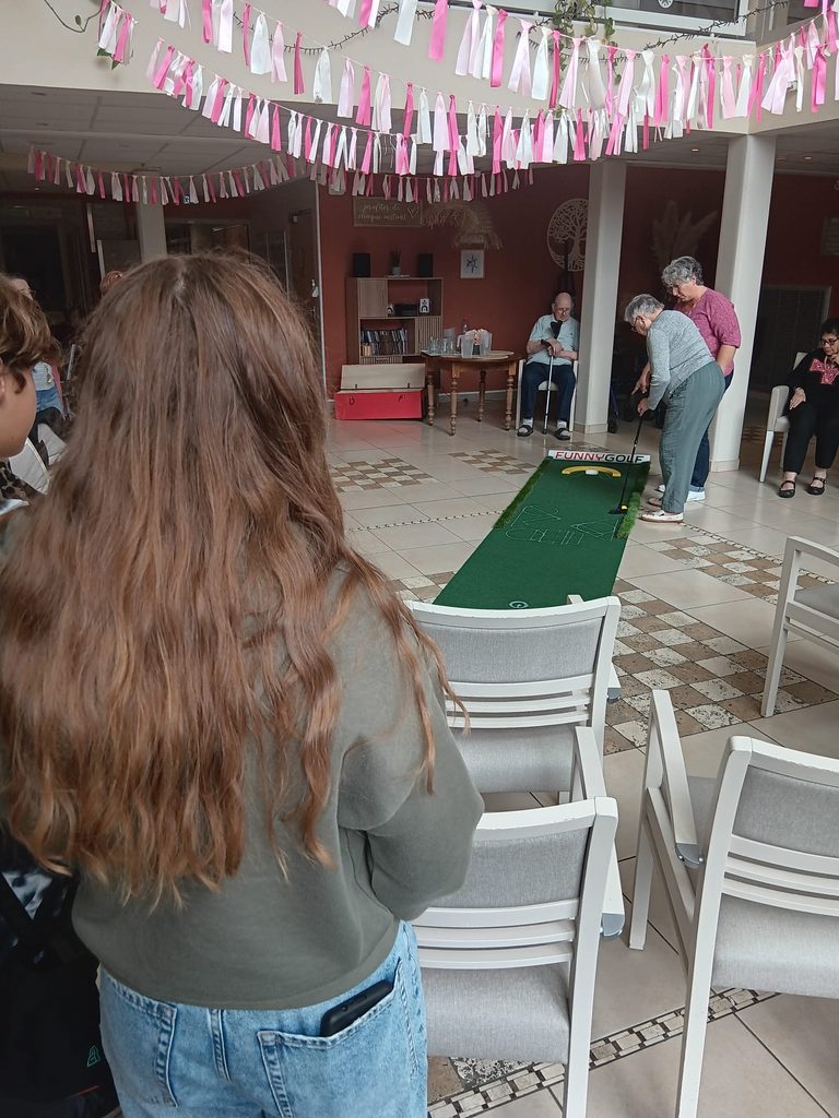 Un groupe joue au mini-golf intérieur avec un parcours "funny golf", sous une décoration festive avec guirlandes.