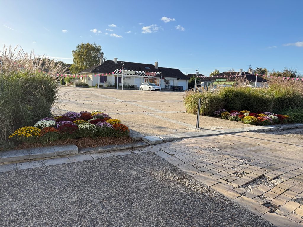 Pavé menant à un parking avec fleurs colorées et bâtiments en arrière-plan sous ciel dégagé.