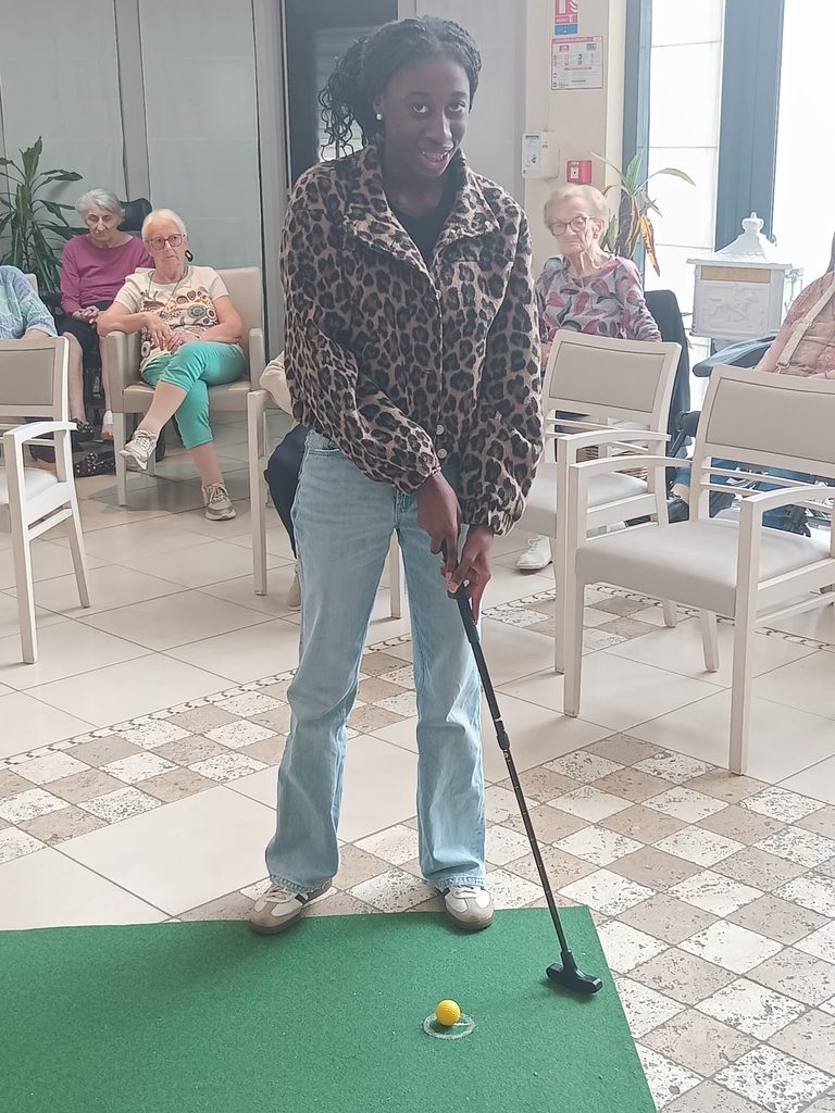 Jeune femme souriante jouant au mini-golf en intérieur, entourée de spectateurs assises.
