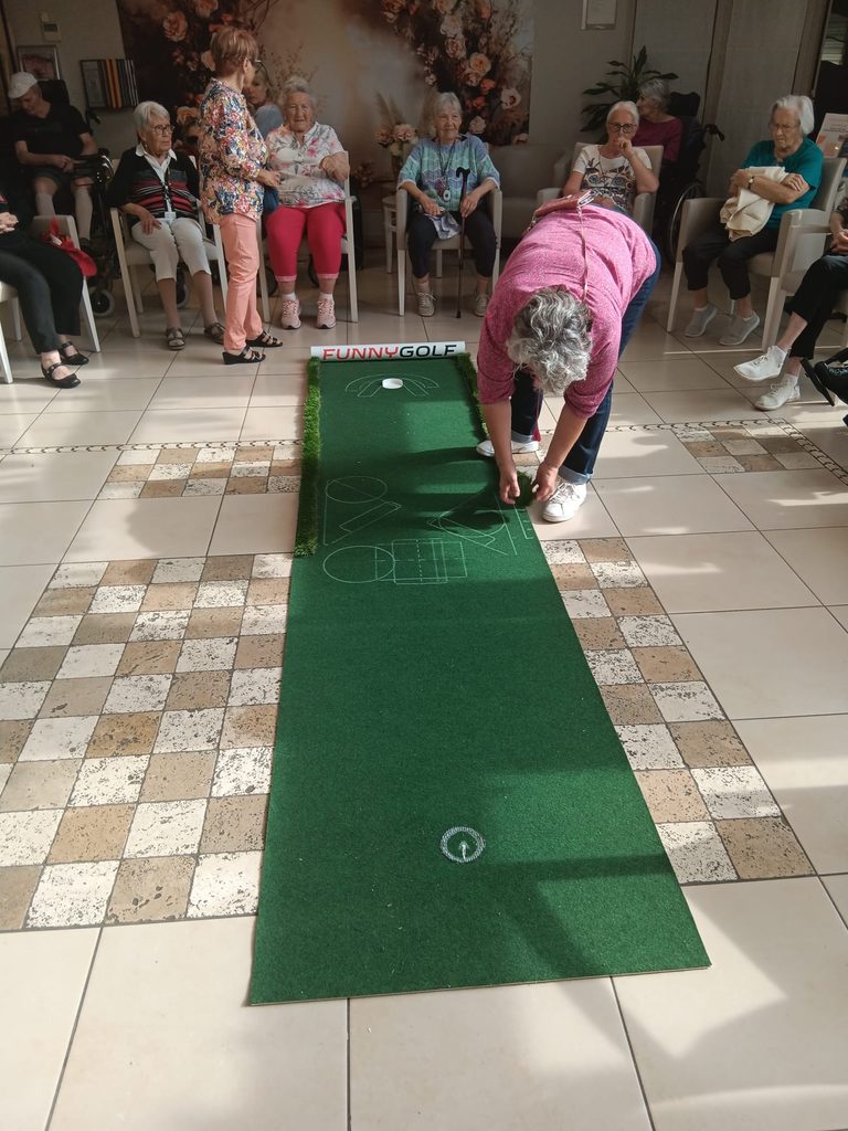 Un groupe joue au mini-golf intérieur, une personne lance une balle sur un parcours vert avec obstacles.