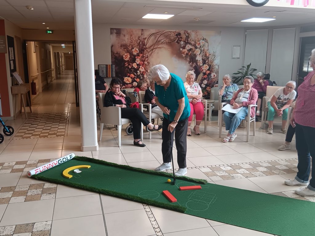 Personnes âgées jouant au mini-golf intérieur, observant une partie sur un parcours vert avec obstacles.