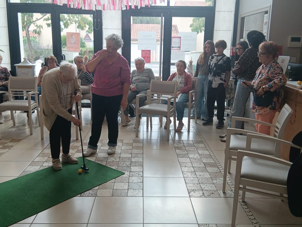 Groupe de personnes jouant au mini-golf intérieur, certaines debout avec cannes, d’autres assises observant.
