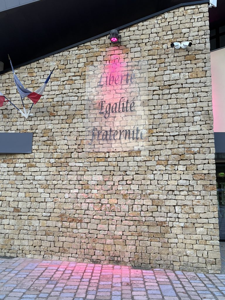 Maison en pierre avec inscription lumineuse « Liberté, Égalité, Fraternité » et drapeau français.