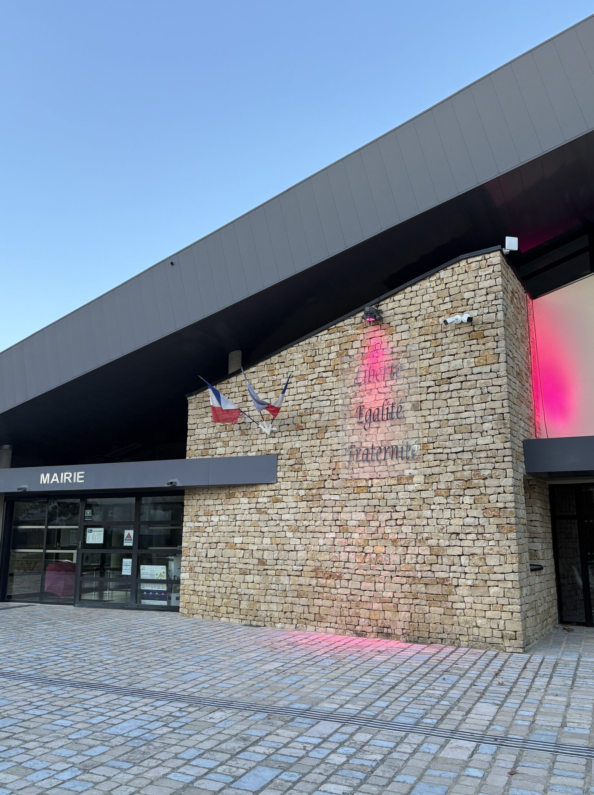 Mairie moderne avec façade en briques, affichant "Liberté, Égalité, Fraternité" et drapeau français, entrée vitrée.